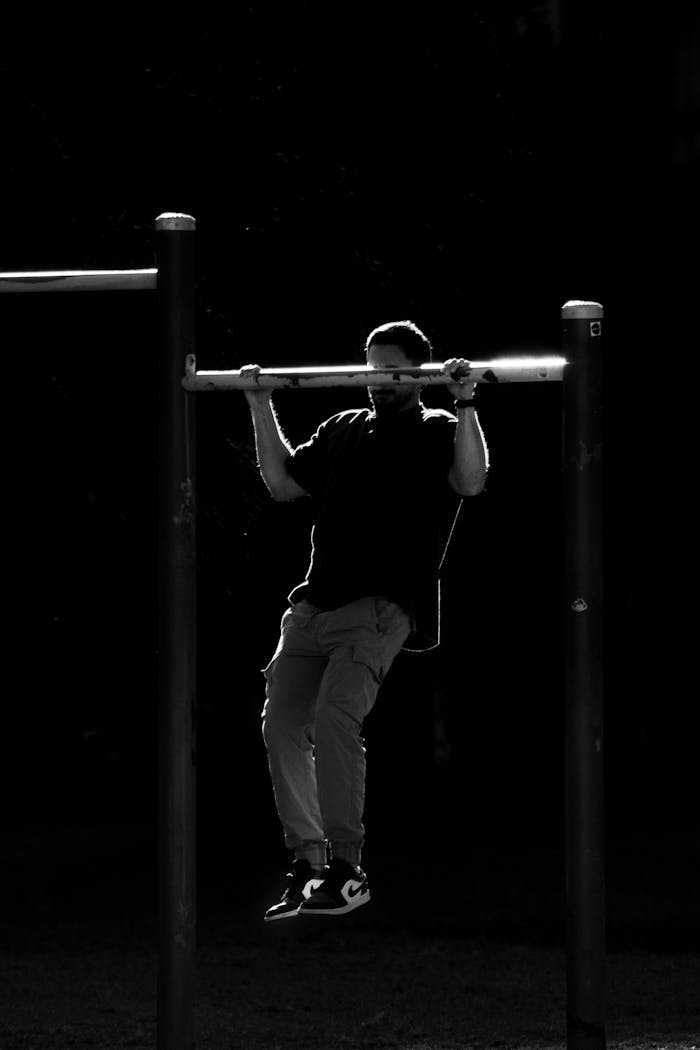 A man doing pull-ups on an outdoor gym set in a striking black and white contrast image.