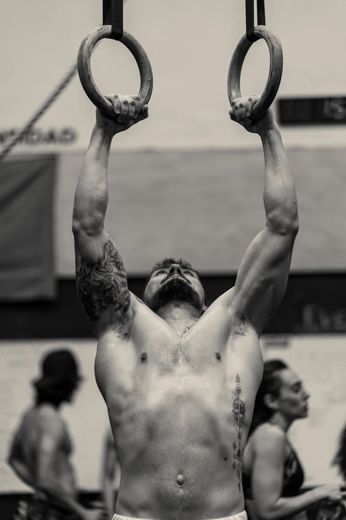 Muscular man shows strength during ring exercise in gym setting.