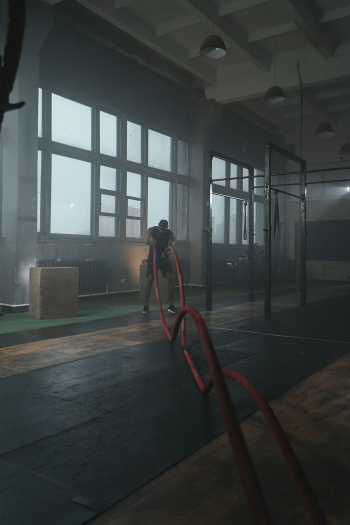 A man engaged in a rigorous workout using battle ropes in a dimly lit gym setting.